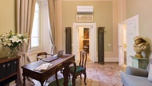 Un coin repas avec une table en bois, des chaises et un ordinateur portable. On aperçoit un vase rempli de fleurs sur une petite table d’appoint, ainsi qu’un buste sculpté posé sur un piédestal.
