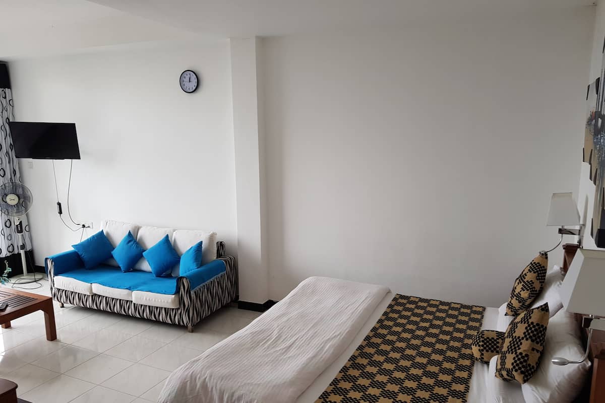 A hotel room with a bed, a sofa, a clock, and a lamp.