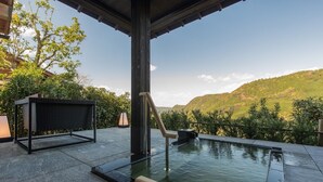 An infinity pool with a waterfall feature, surrounded by a covered patio area with a wicker chair and a table.