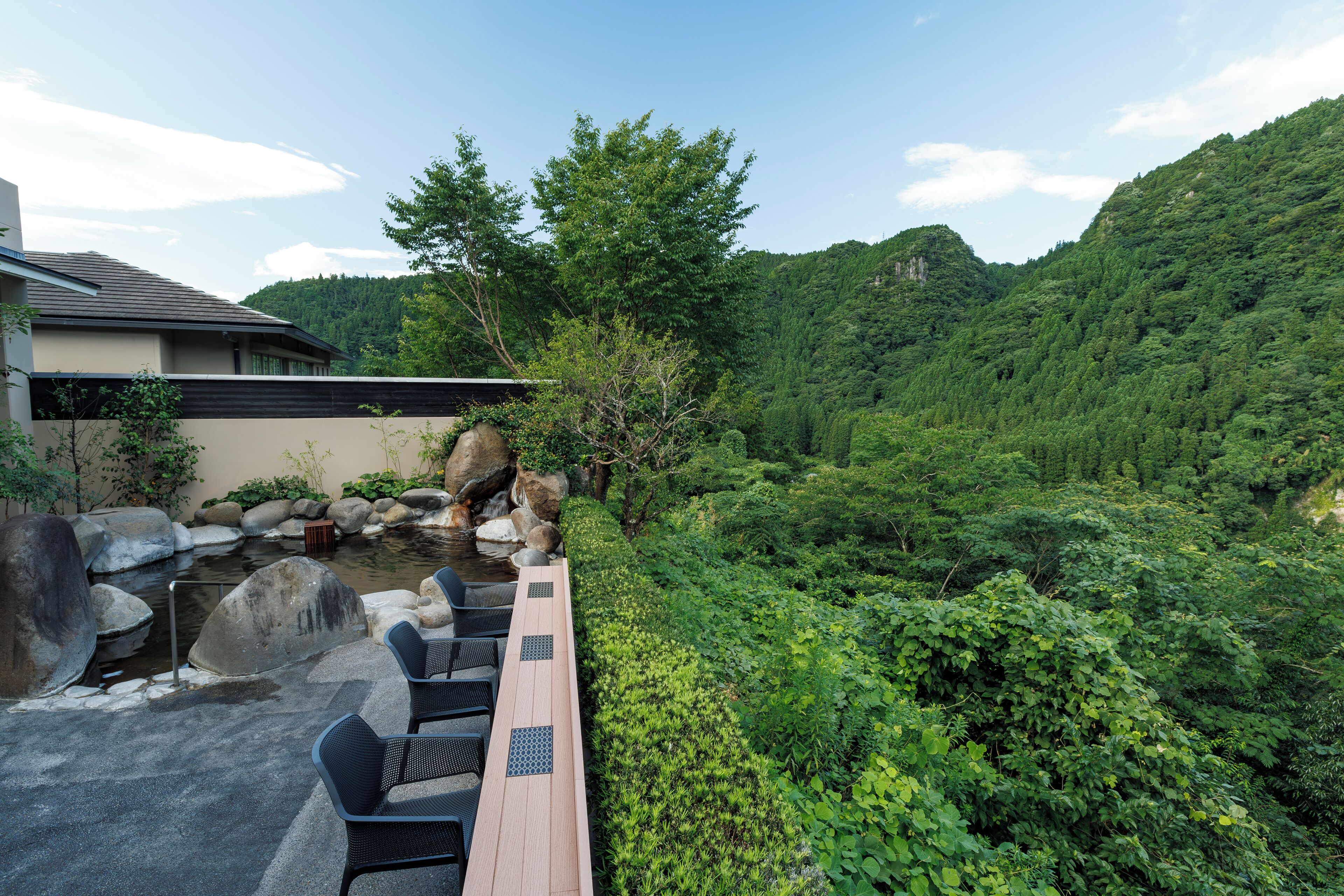 A serene outdoor seating area with a wooden deck, black chairs, and a small pond with rocks and a waterfall.