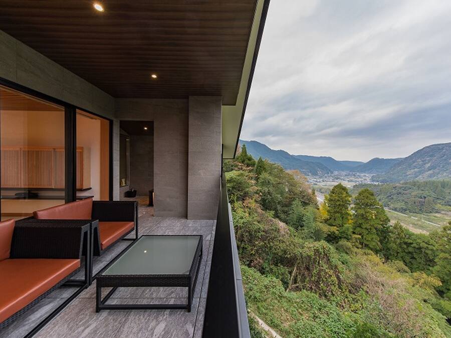 Un espace extérieur moderne, aménagé avec des sièges et doté d’une balustrade en verre offrant une vue sur un paysage montagneux.