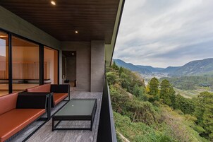 Un área de estar exterior moderna con barandilla de vidrio con vista a un paisaje montañoso.