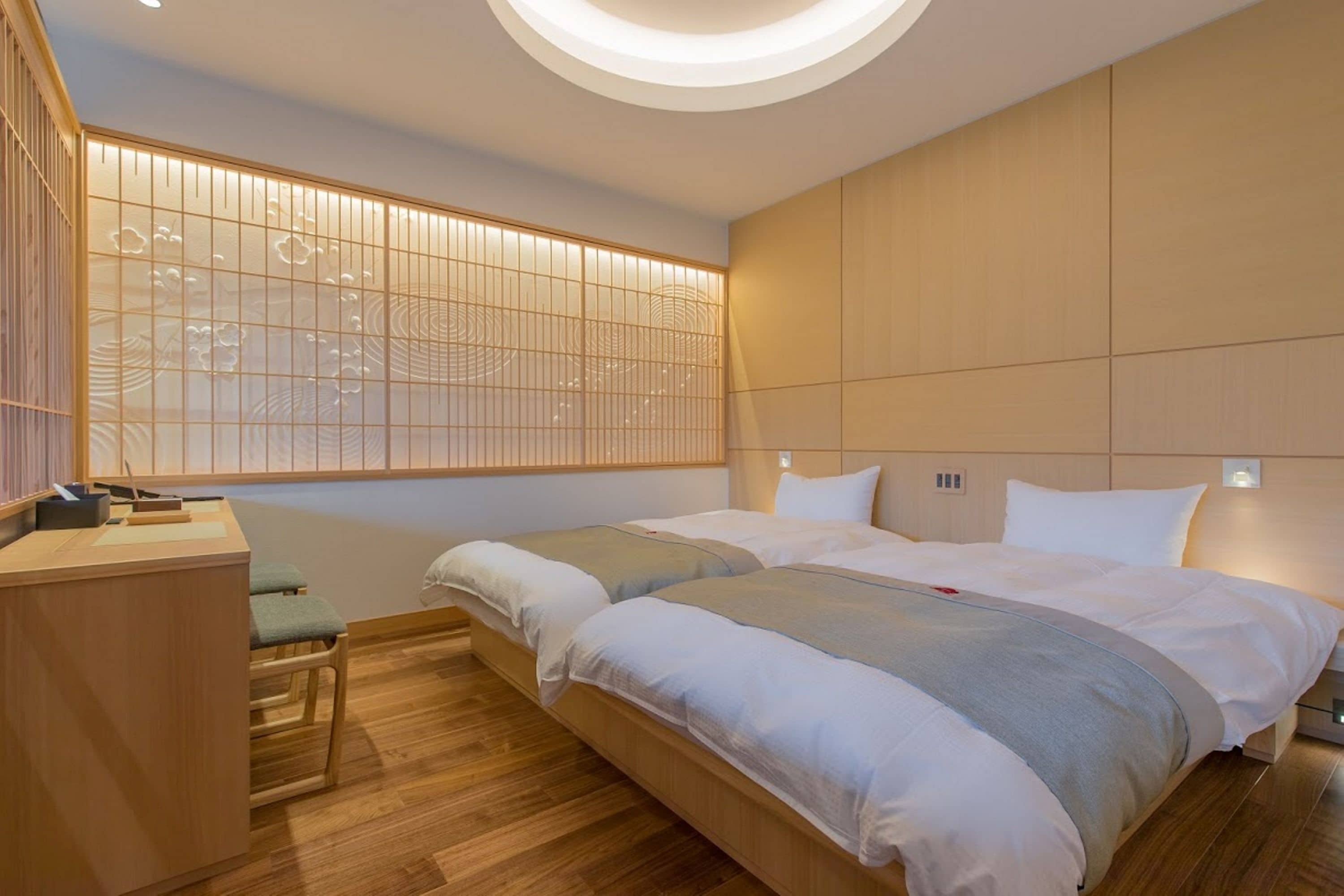 A modern hotel room with two beds, a desk, and a traditional Japanese-style partition.