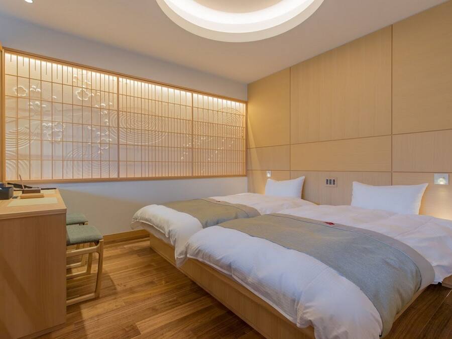 Une chambre d’hôtel moderne équipée de deux lits, d’un bureau et d’une cloison de style japonais traditionnel.