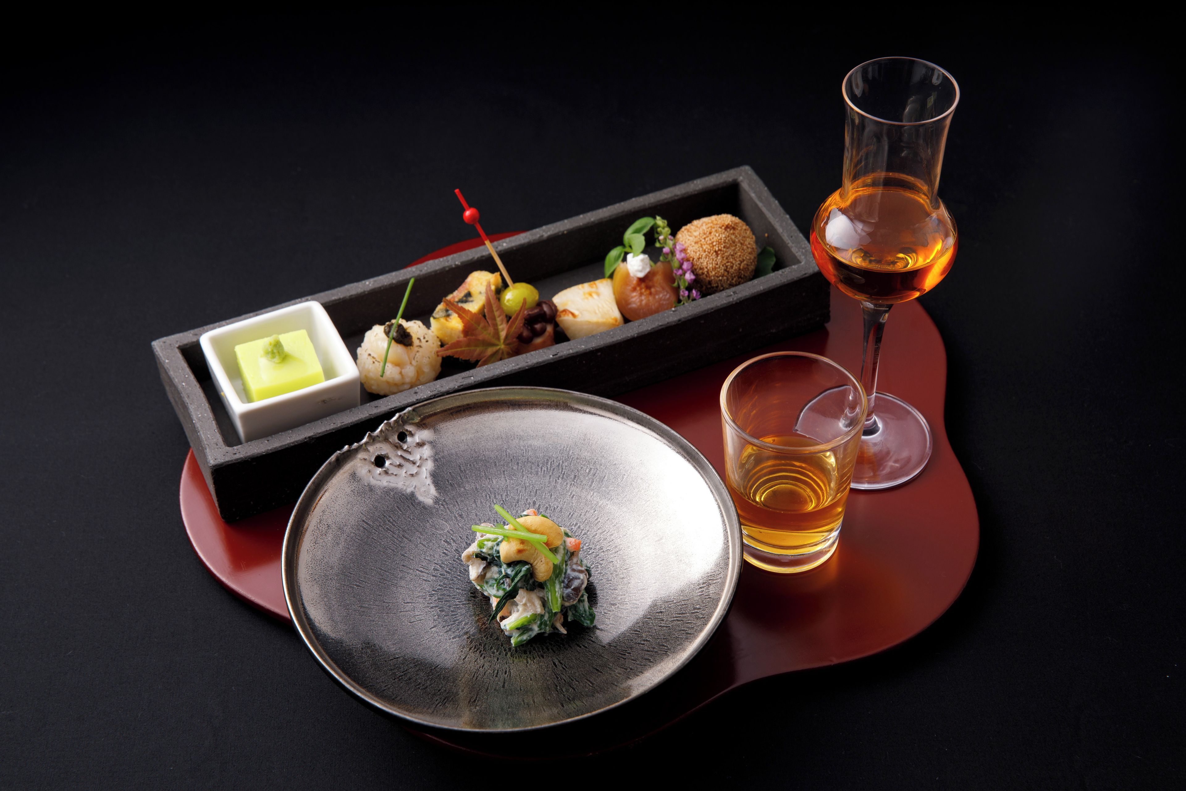 A dining table with a black plate, a rectangular dish with food, and a glass of red wine.