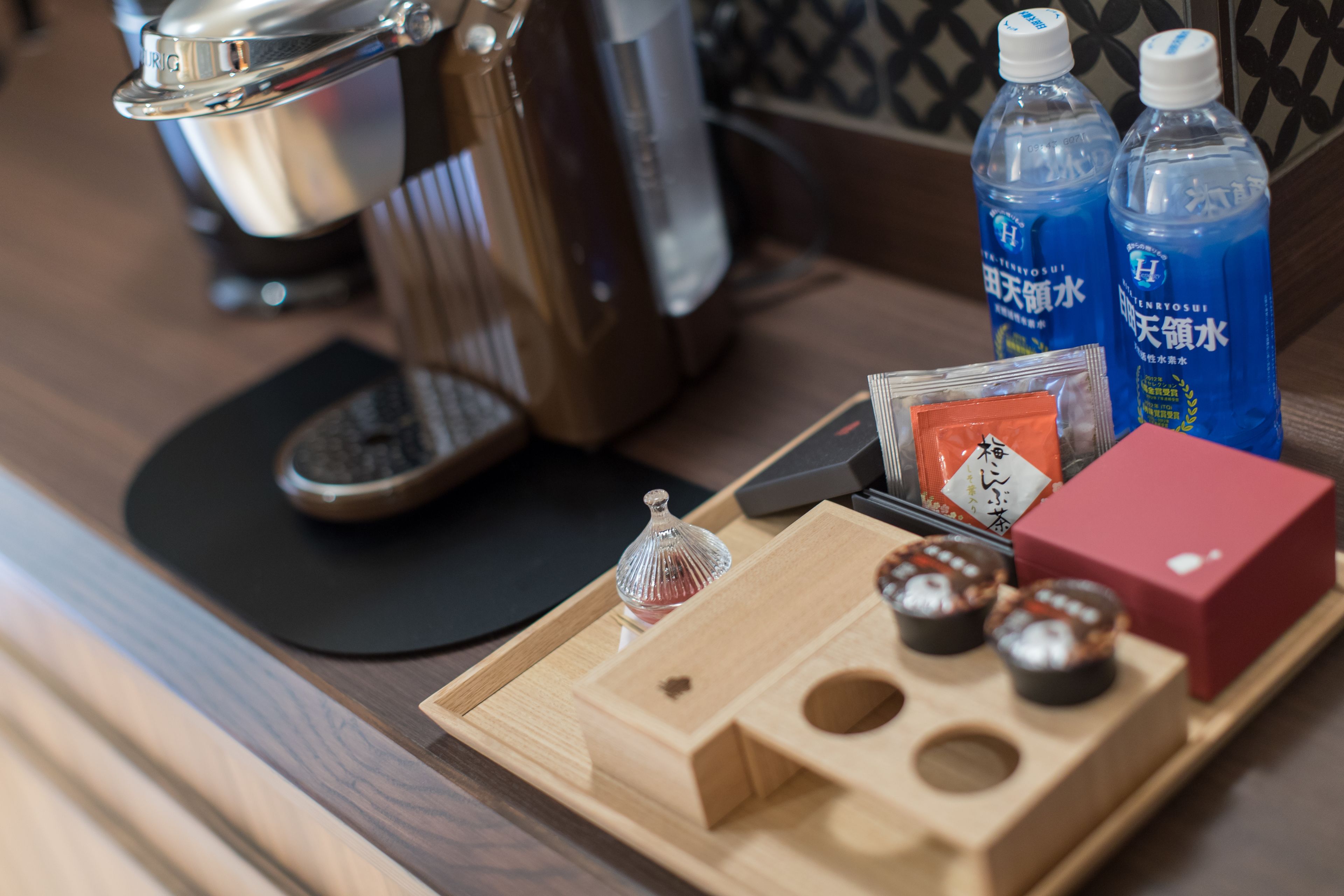 Una bandeja de madera con bolsitas de té, un vaso y una caja roja sobre una mesa.