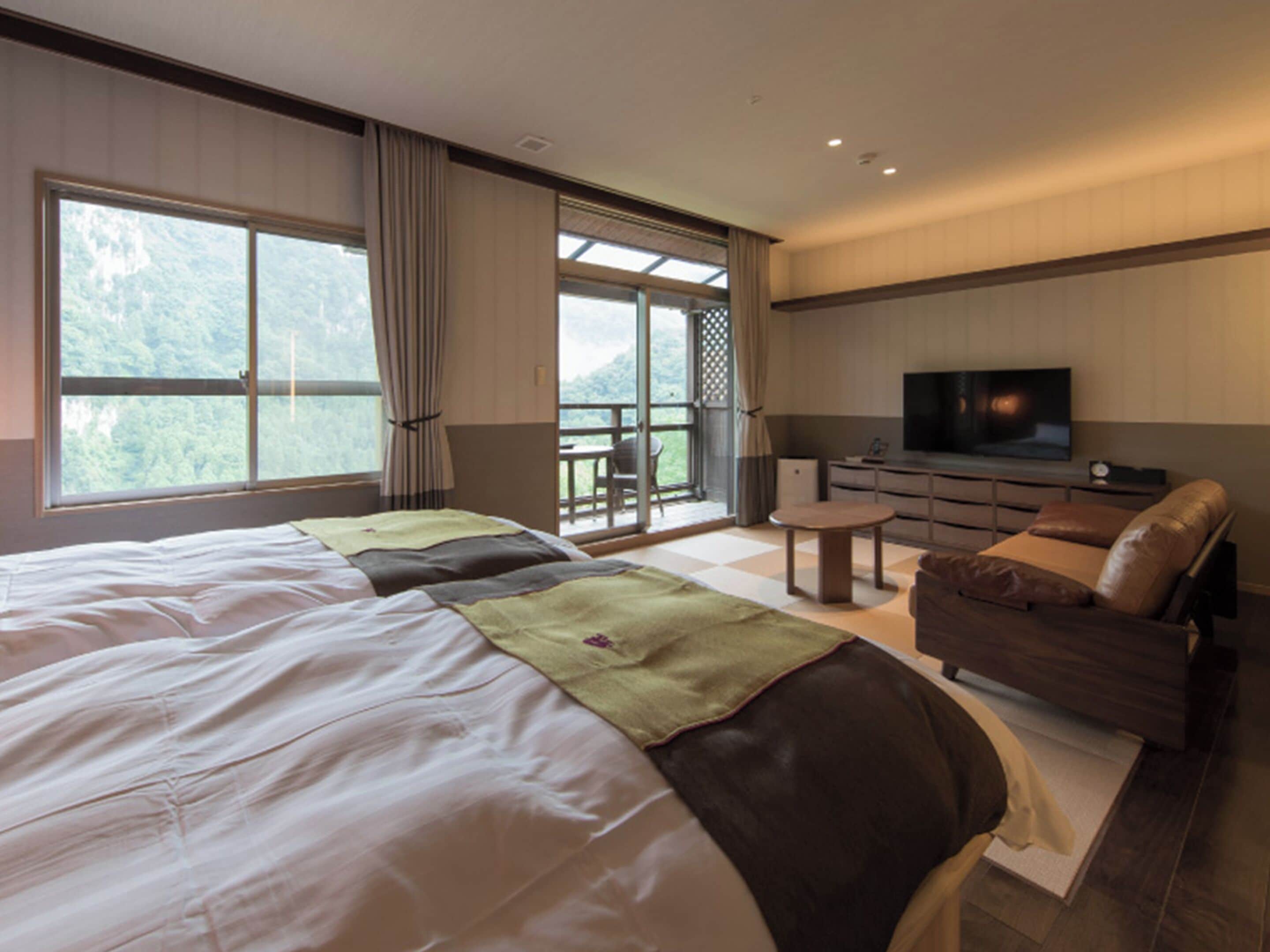 A bedroom with a large bed, a sofa, a TV, and a balcony with a view of the mountains.
