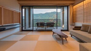 A modern interior with a large sliding glass door leading to a balcony, a sofa, a table, and a TV on a shelf.