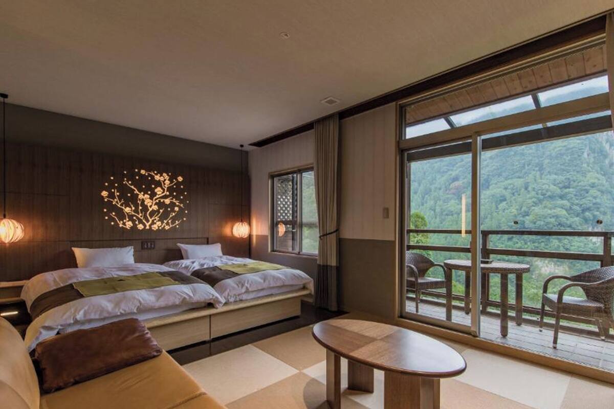 Une chambre d’hôtel moderne, dotée d’un grand lit, d’un canapé, d’une petite table et d’un balcon offrant une vue sur la forêt.