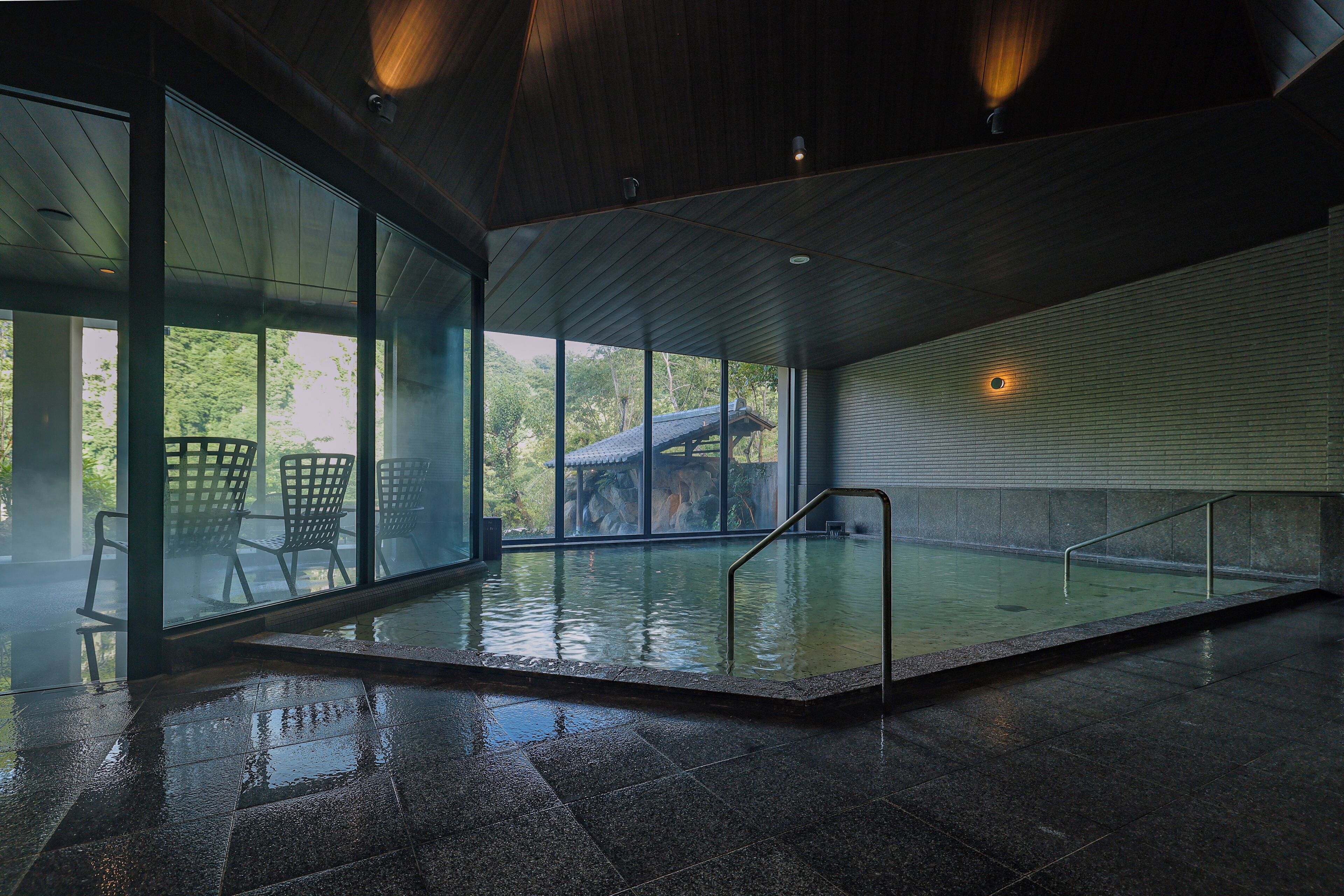 Una piscina interna con pareti in vetro, ringhiere in metallo e pavimento piastrellato.