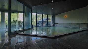 Una piscina interna con pareti in vetro, ringhiere in metallo e pavimento piastrellato.