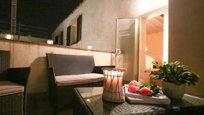 Un espace extérieur aménagé avec des meubles en osier, une table en verre, un chandelier et un pot de fleurs.