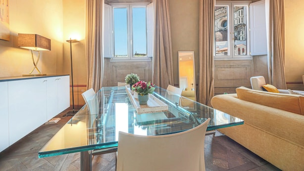 Un salon moderne avec une table à manger en verre, un canapé beige et une vue sur le paysage urbain par la fenêtre.