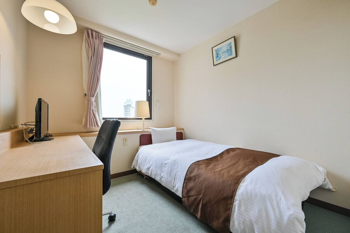 A hotel room with a bed, desk, chair, and a window with curtains.