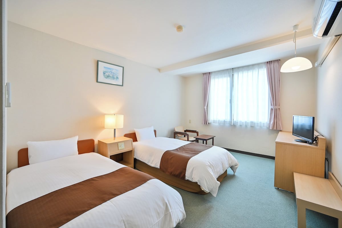 A hotel room with two beds, a desk, a chair, a television, and a window with curtains.