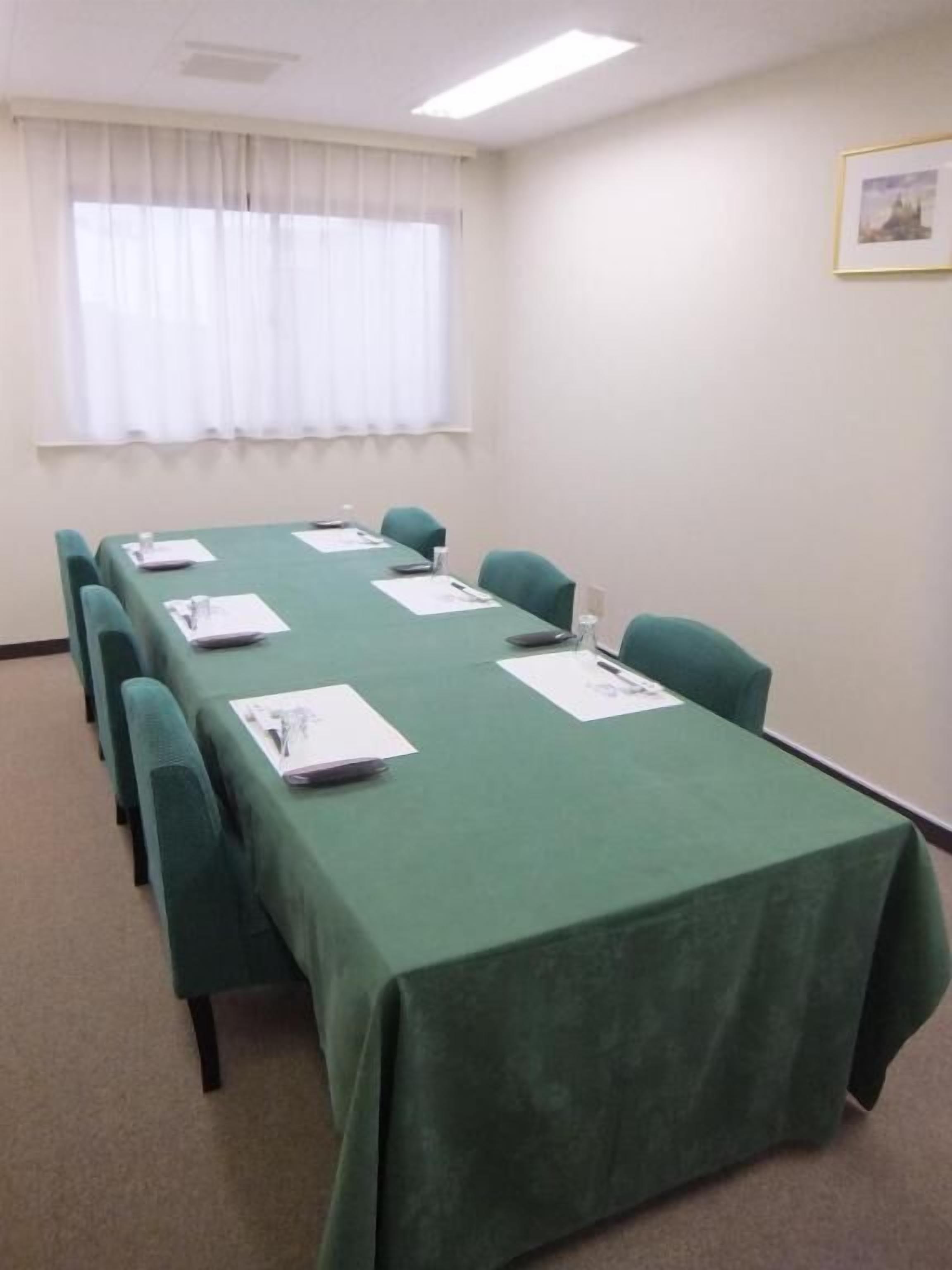 A conference room with a long table, chairs, and a window with curtains.