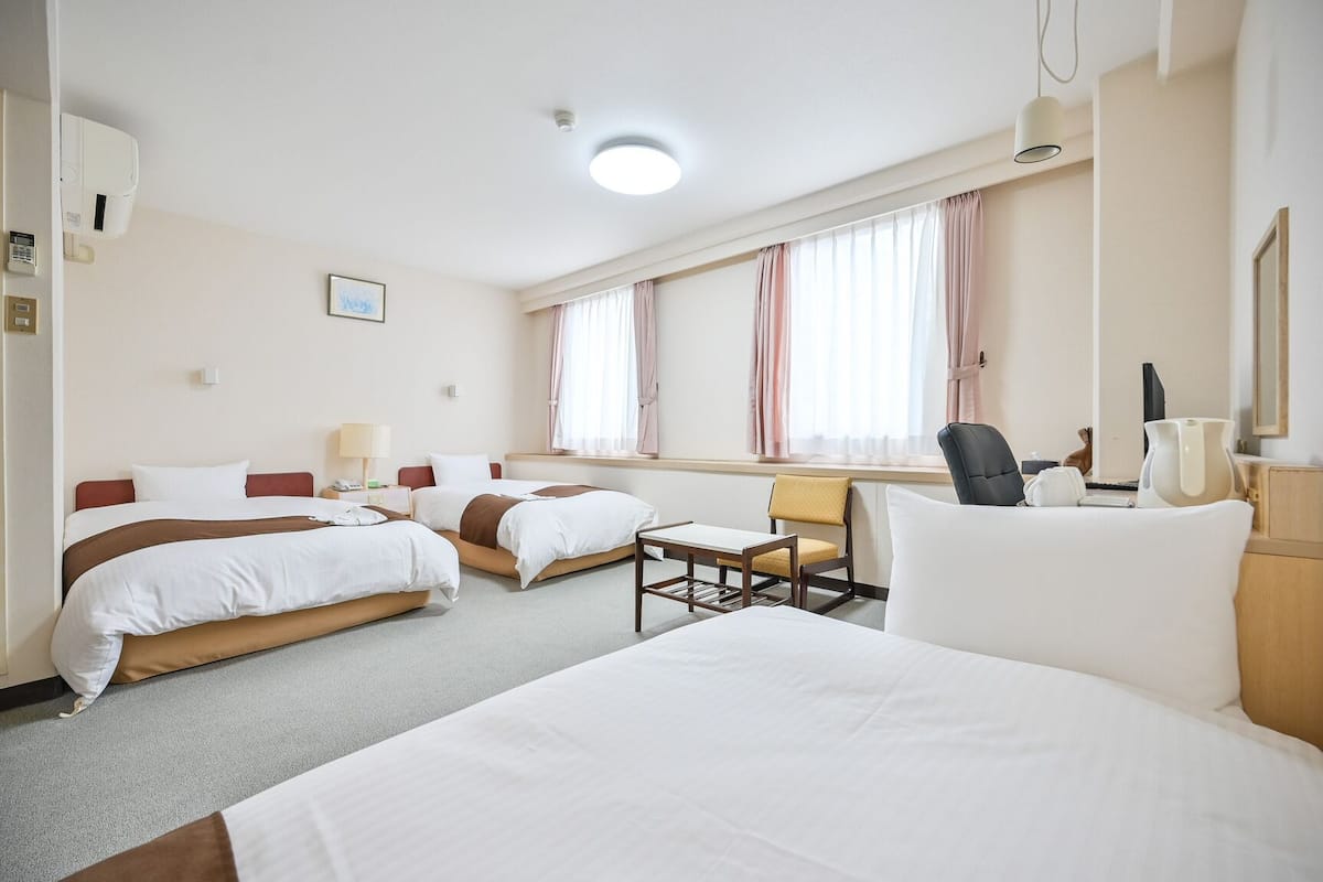 A hotel room with two beds, a desk, a chair, a lamp, and a window with curtains.
