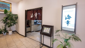 L’intérieur d’un restaurant, avec un présentoir à menus, des plantes en pot et une vue sur la cuisine par une porte ouverte.