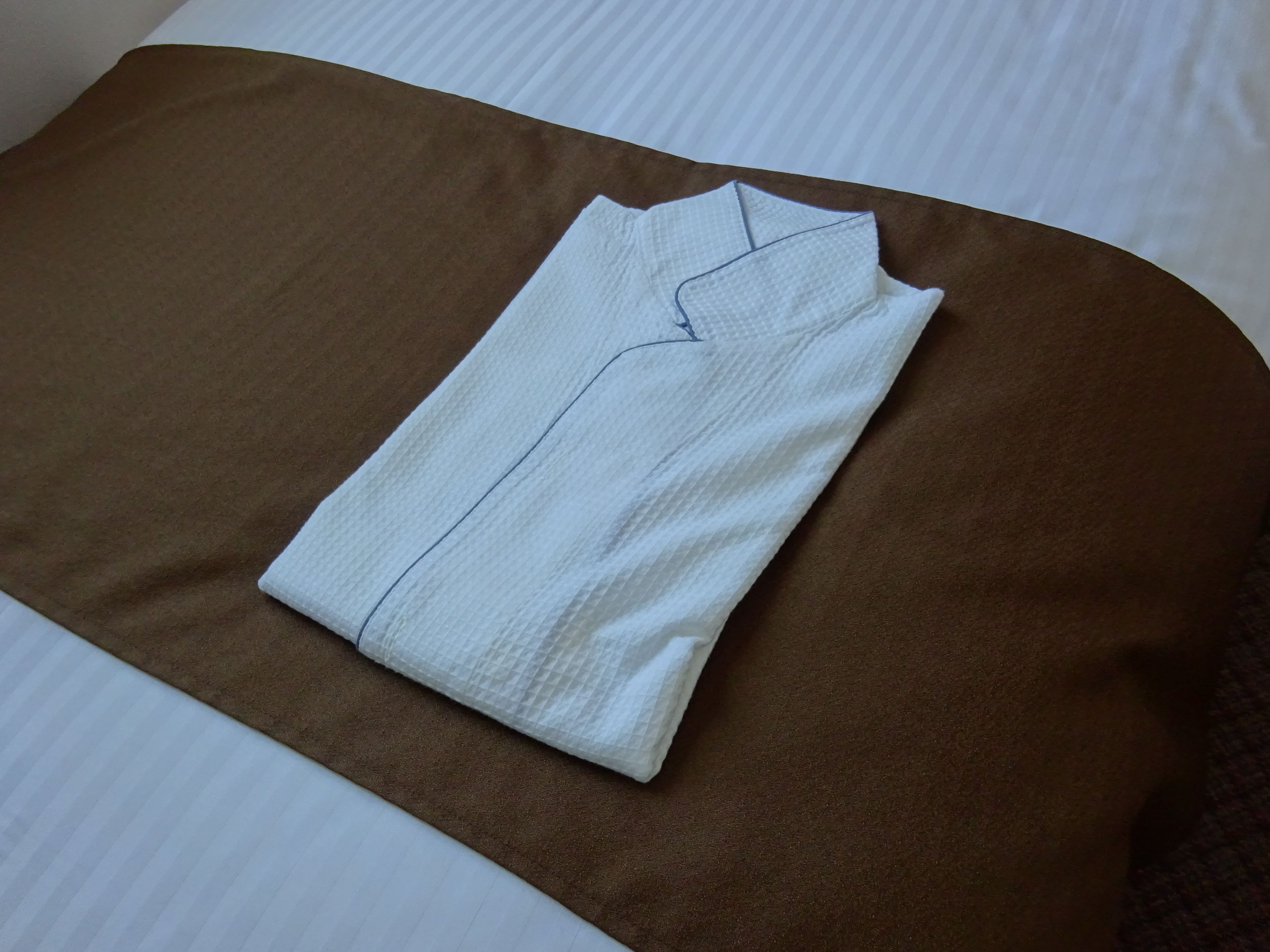 Una camisa blanca bien doblada sobre un cojín marrón en una cama.