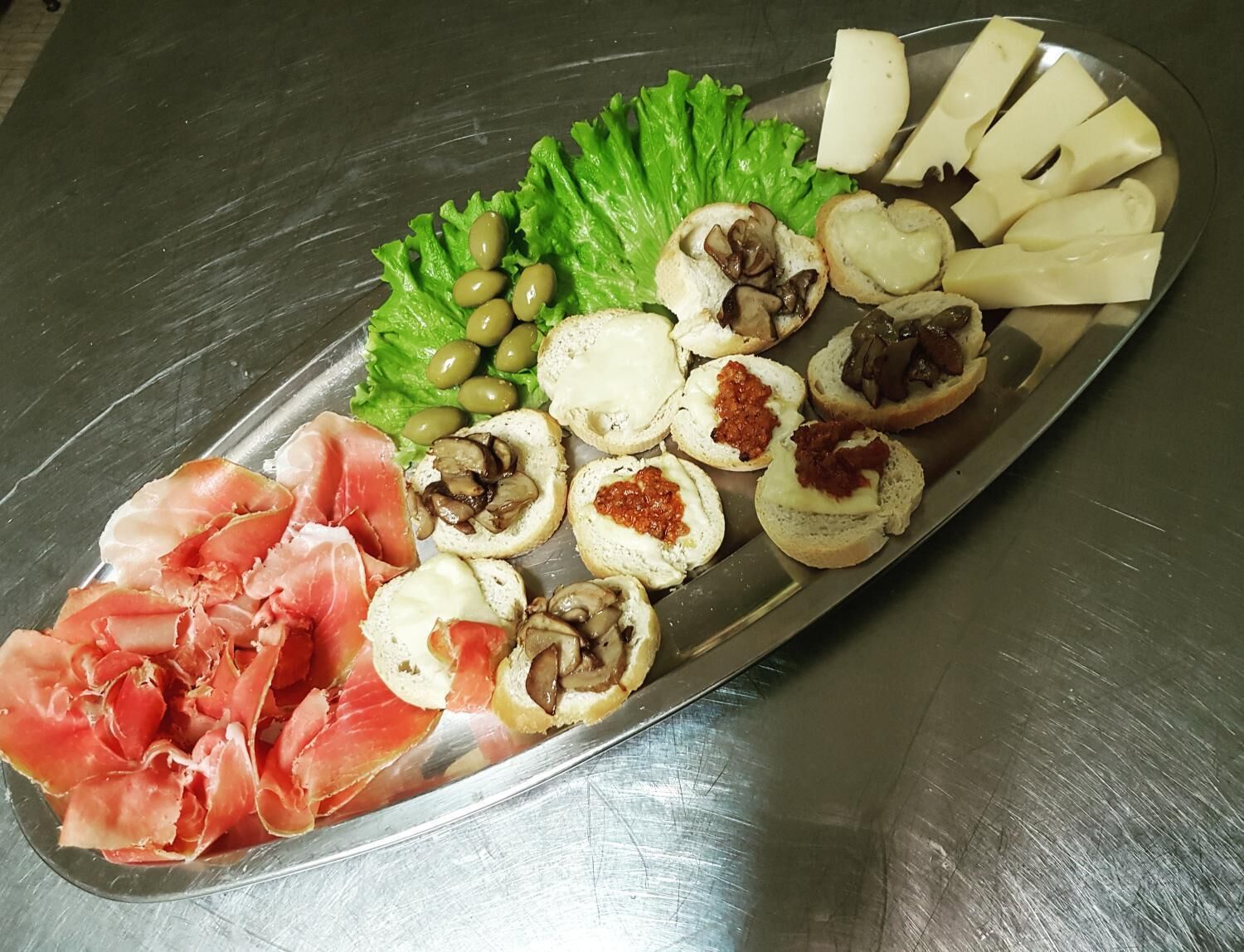 A platter with various food items including olives, cheese, mushrooms, and prosciutto.