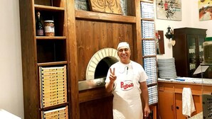 A kitchen with a wood-framed pizza oven, shelves with pizza boxes, and a person wearing a 'Pizzoli' apron. - Albergo Ristorante Poli (San Benedetto Val di Sambro)