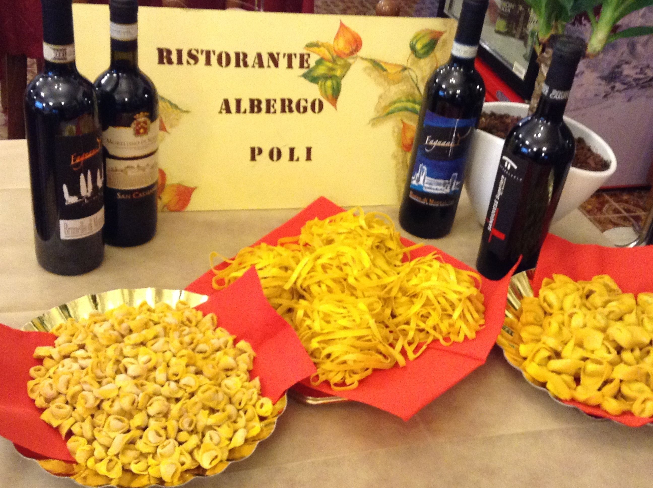 Taula amb tres plats de pasta, dues ampolles de vi i un cartell que diu "RISTORANTE ALBERGO POLI".