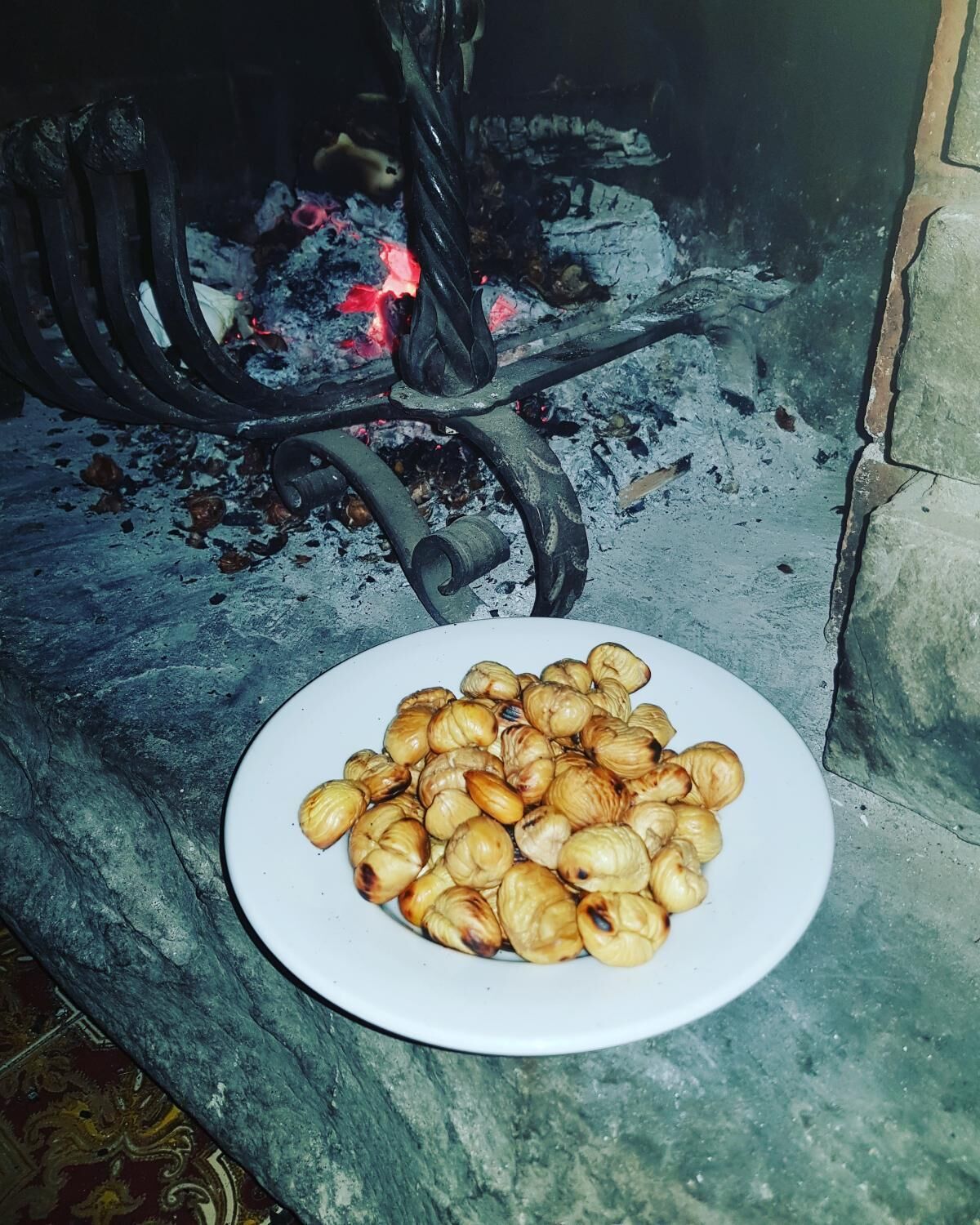 Un plato de castañas asadas sobre un banco de piedra cerca de una chimenea con una rejilla de metal.