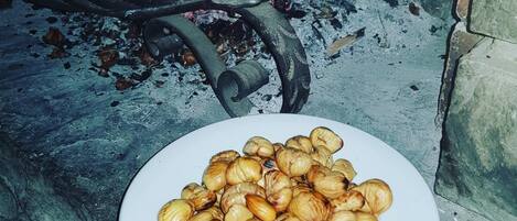 Un plato de castañas asadas sobre un banco de piedra cerca de una chimenea con una rejilla de metal.