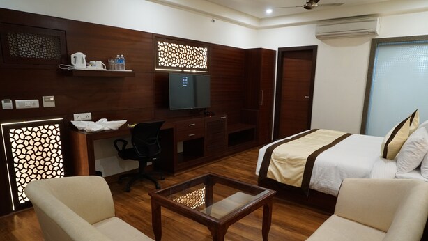 Ein Hotelzimmer mit einem Bett, zwei Sesseln, einem Schreibtisch mit Computer, einem Fernseher und einer Minibar.