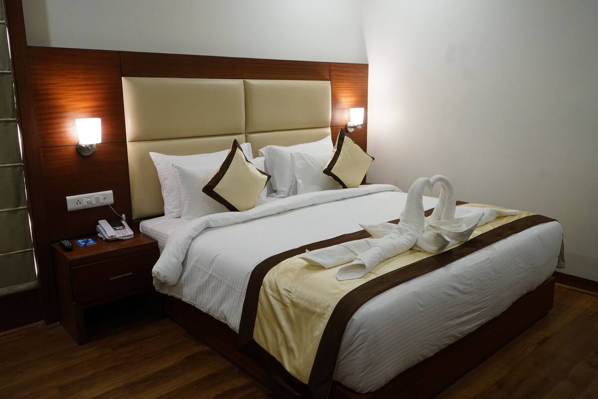 A hotel room with a large bed, a bedside table with a phone, and wall-mounted lights.