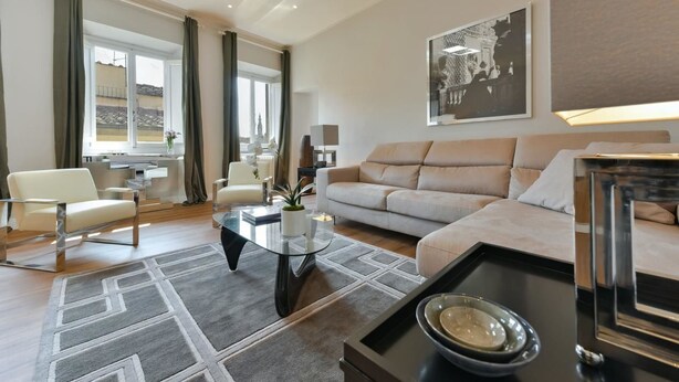 A modern living room with a sofa, armchairs, a glass coffee table, and a dining table with a tray. - Santa Croce Deluxe (Florence)