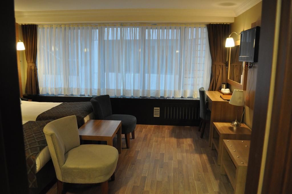 Een hotelkamer met een bed, een bank, een kleine tafel, een stoel, een bureau, een televisie en een raam met gordijnen.
