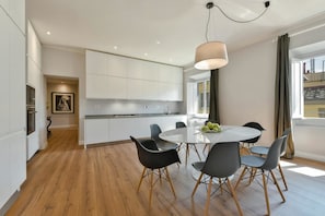 Une cuisine moderne avec des meubles blancs, une table de salle à manger ronde entourée de chaises noires et un luminaire suspendu.