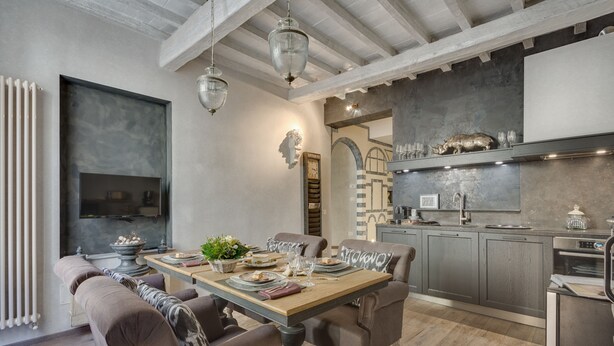 A modern kitchen with a dining area, featuring a wooden table, grey cabinets, and a built-in oven. - Signoria Art (Florence)