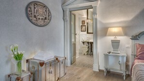 A room with a bed, a nightstand, a lamp, and a wall-mounted picture. There is a door leading to another room. - Signoria Art (Florence)