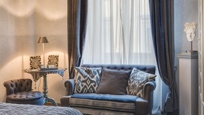 A cozy room with a sofa, armchair, and a small table with a lamp and decorative items. - Signoria Art (Florence)