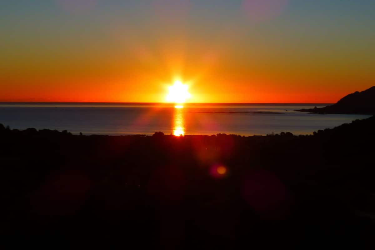 Een zonsondergang boven een rustige zee, met een bergketen in de verte als silhouet.