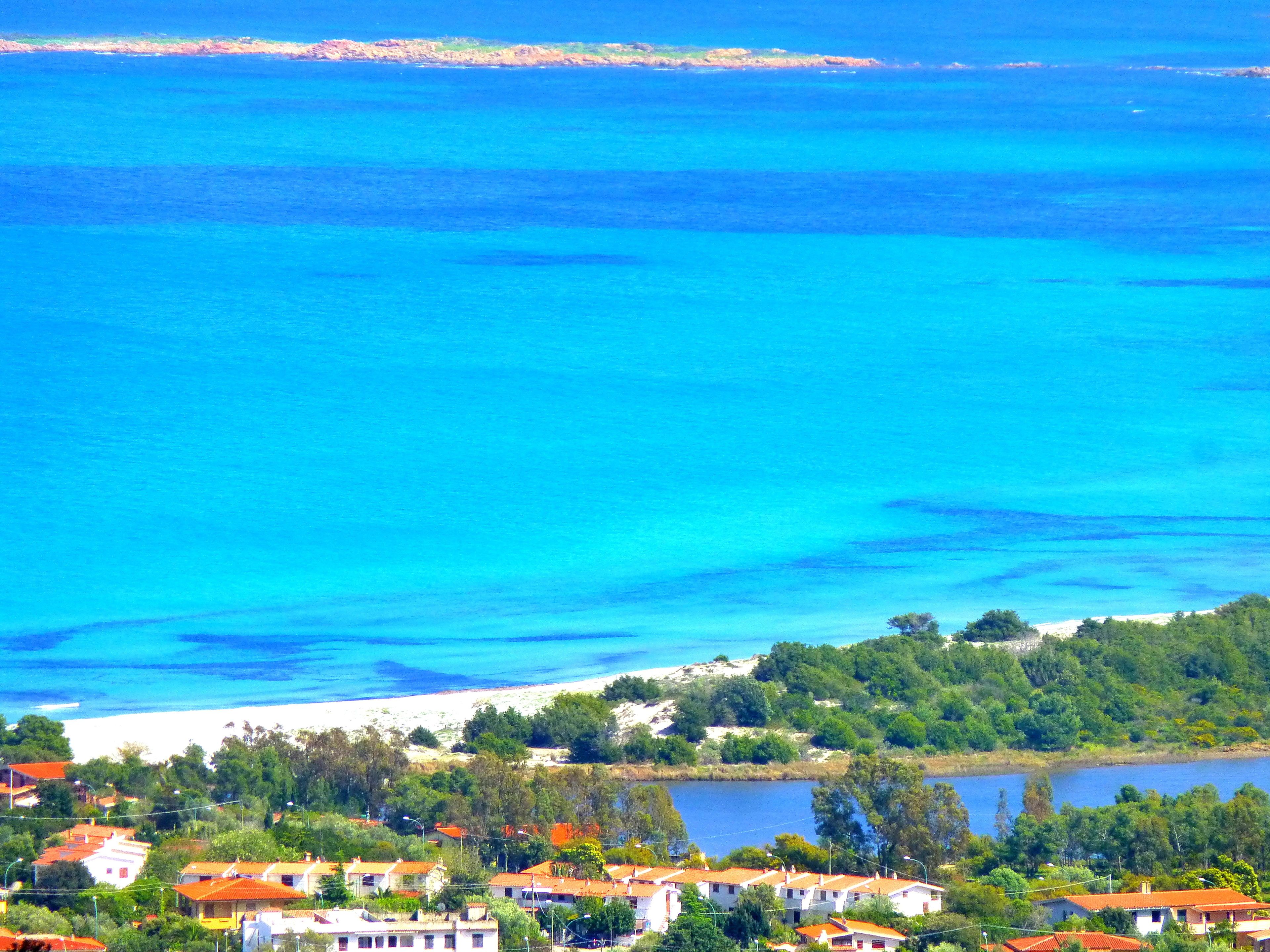 Ein Küstendorf mit weißen Häusern und roten Dächern, einem Sandstrand und einem klaren, blauen Meer.