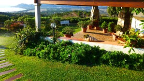A garden with a stone bench, potted plants, and a clear view of the landscape. - Comino Alto Agriturismo e  Appartamenti (Siniscola)