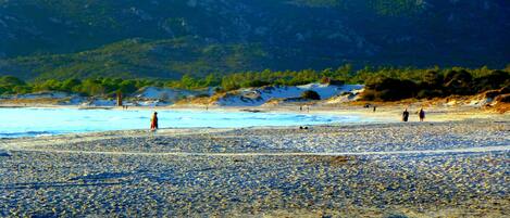 Una playa con piedras, algunas personas y colinas al fondo.