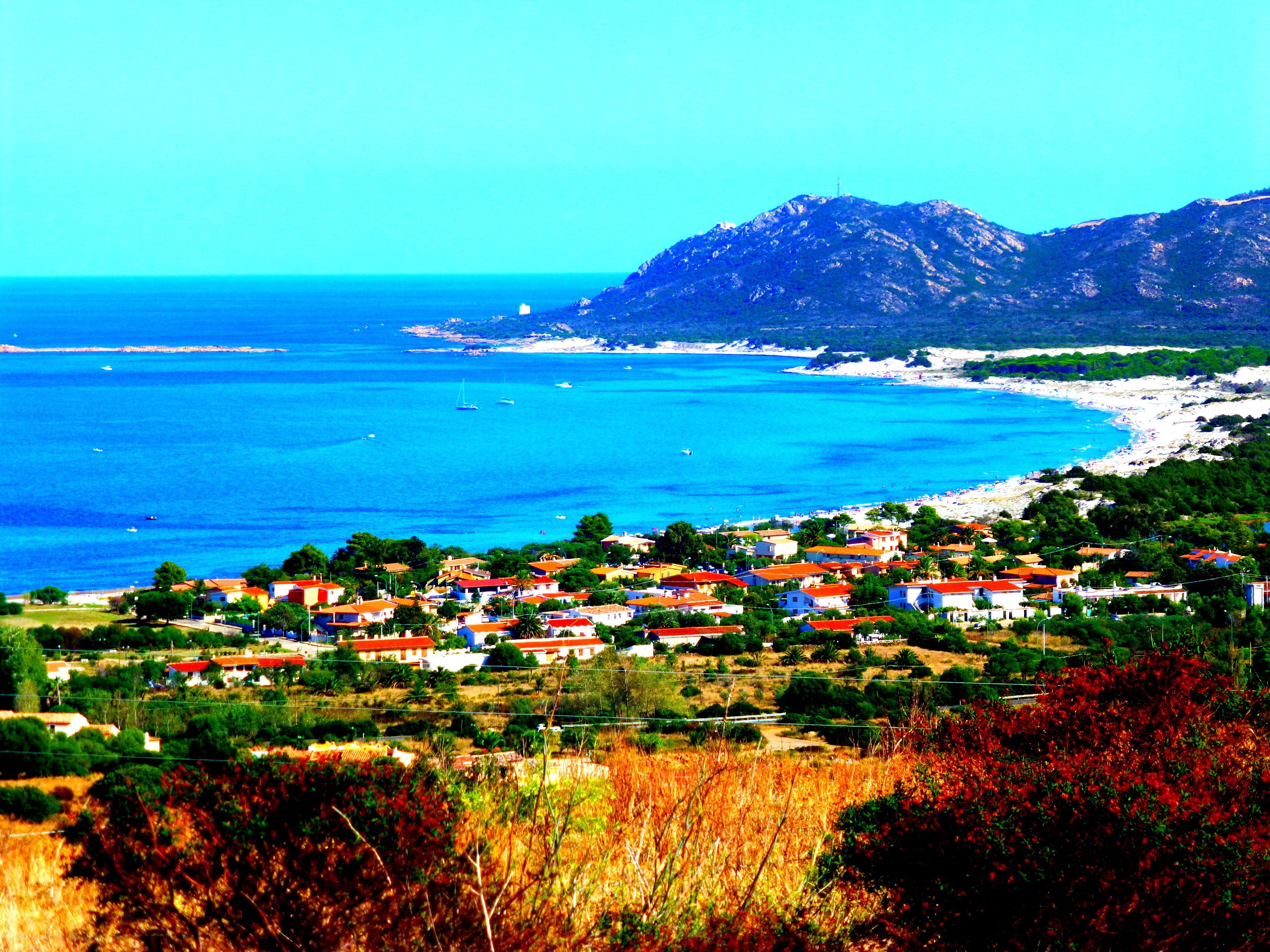 Un pueblo costero con casas, una playa y una montaña al fondo.