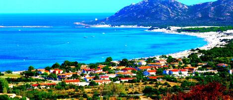 Un pueblo costero con casas, una playa y una montaña al fondo.