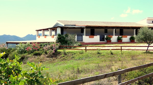 Um edifício de dois andares com telhado de cerâmica, varanda e um jardim com plantas floridas.
