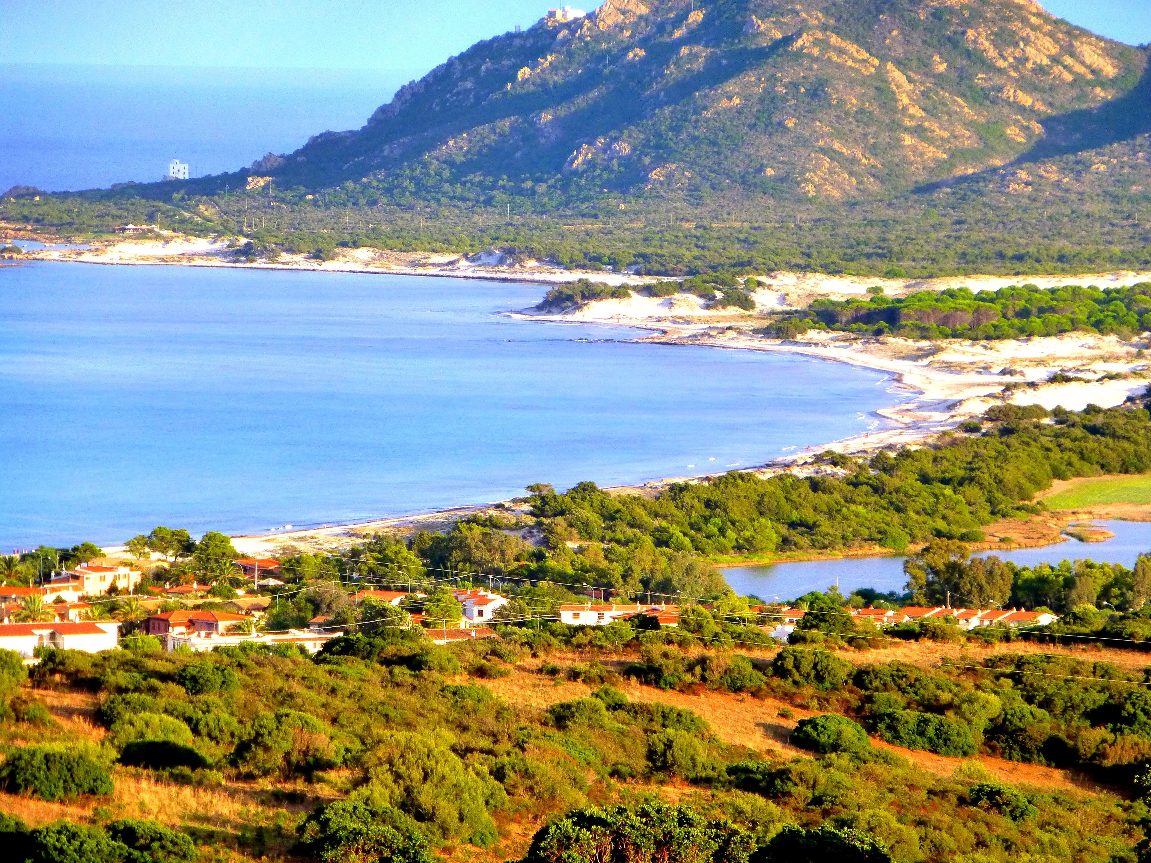 A coastal landscape with a mountain, a beach, and a small settlement with houses.