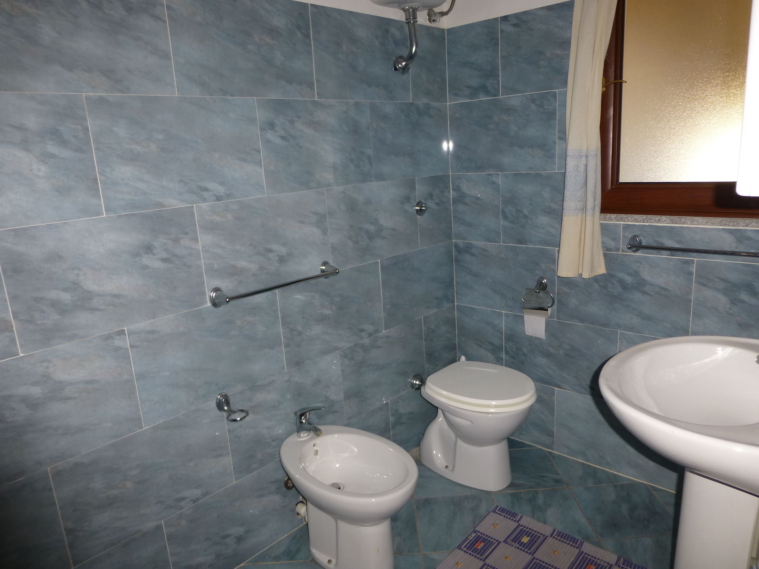 Un baño con azulejos azules, una ducha, dos inodoros y un lavamanos.