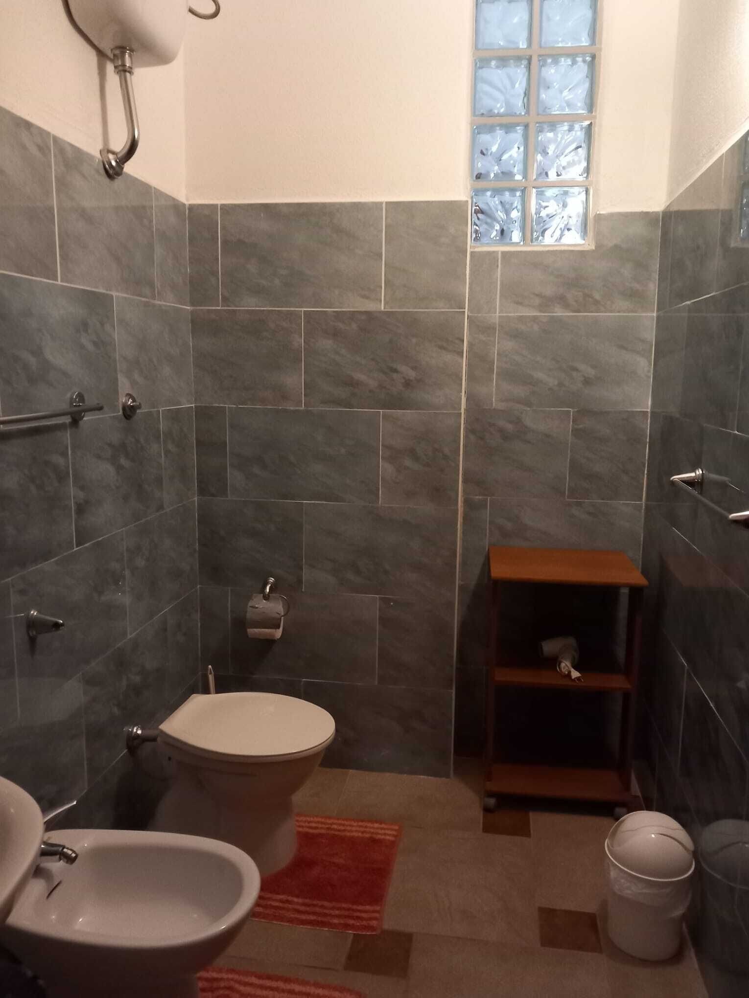 A bathroom with a toilet, bidet, and a small wooden shelf.