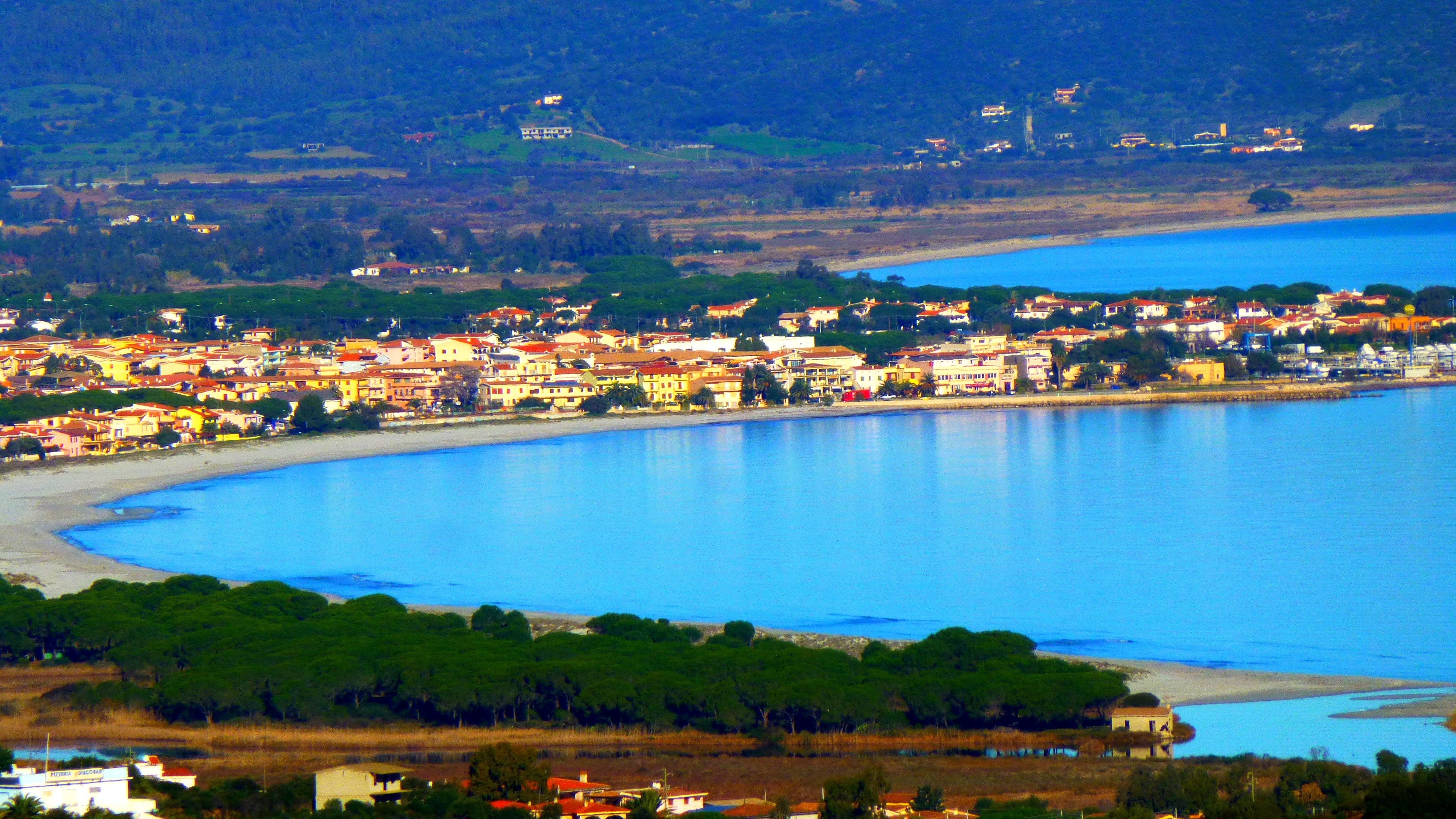 A coastal town with buildings along the waterfront, a sandy beach, and a large body of water.