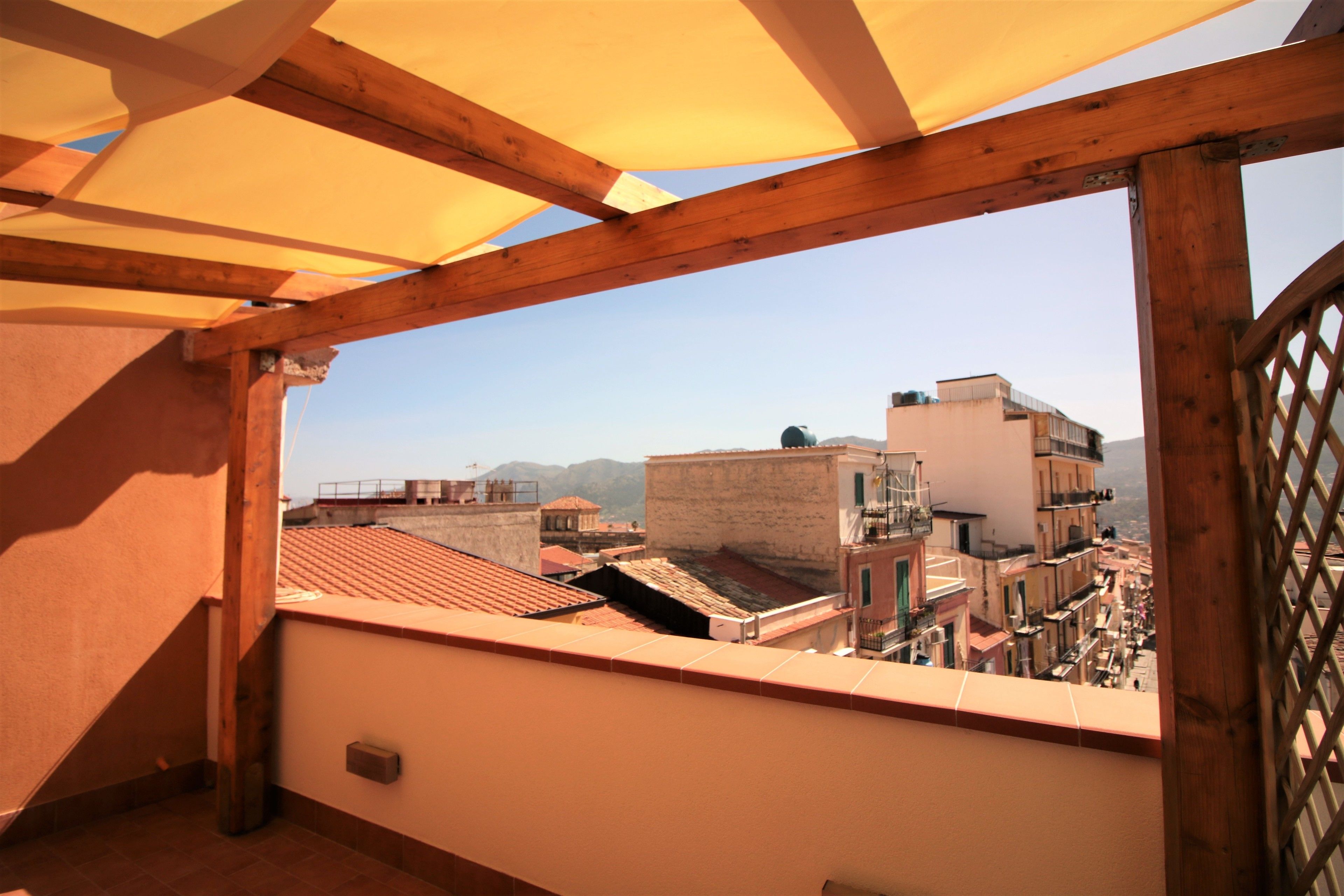 Un balcón con estructura de madera y vistas a un paisaje urbano con edificios y montañas al fondo.