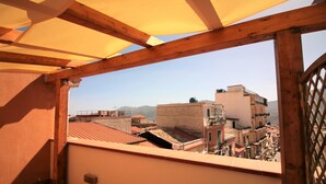 A balcony with a wooden frame and a view of a cityscape with buildings and mountains in the background. - B&B La Rosatea (Monreale)