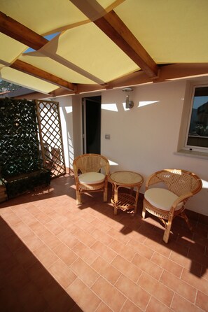 Un patio al aire libre con dos sillones de mimbre y una mesita, vigas de madera y piso de baldosas.